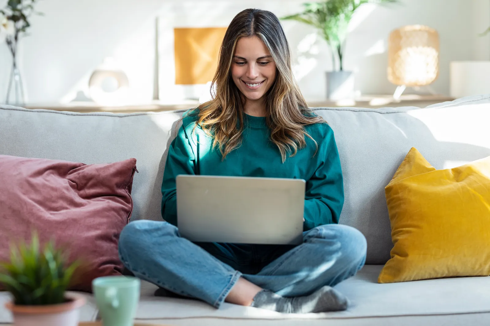 Eine Frau sitzt mit dem Laptop auf dem Sofa.