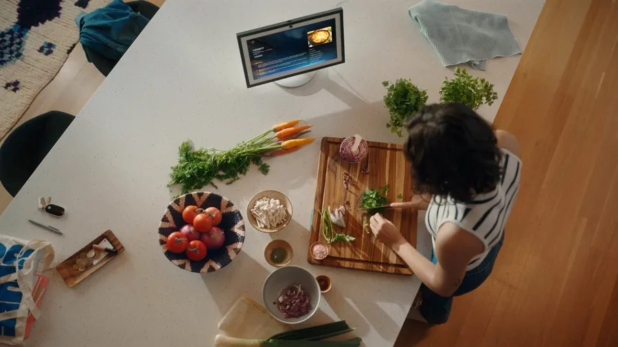 Frau schneidet Kräuter an einem Küchentisch, daneben zeigt ein Echo Show ein Rezept für Lasagne