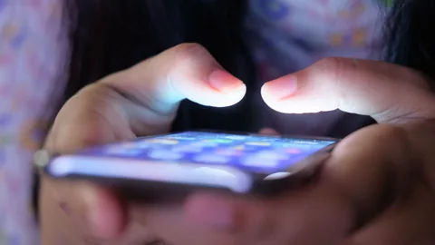 Nahaufnahme von zwei Fingern über dem leuchtenden Bildschirm eines Smartphones in einem dunklen Raum
