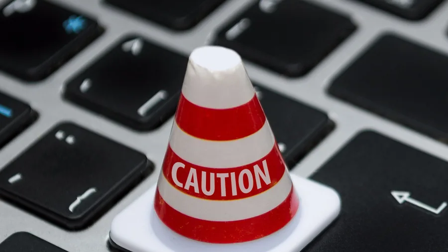 Kleiner rot-weißer Warnkegel mit der Aufschrift Caution auf einer Computertastatur