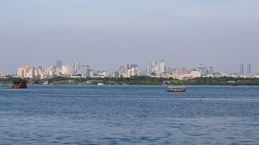 Die Hochhäuser von Hangzhou hinter dem Westsee, davor zwei Holzboote auf dem Wasser; in der Stadt sitzt DeepSeek