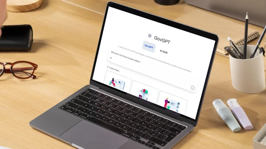 Ein aufgeklappter Laptop auf einem Holztisch zeigt die Startseite von GovGPT mit dem Eingabefeld „Wie kann ich Ihnen heute helfen?“