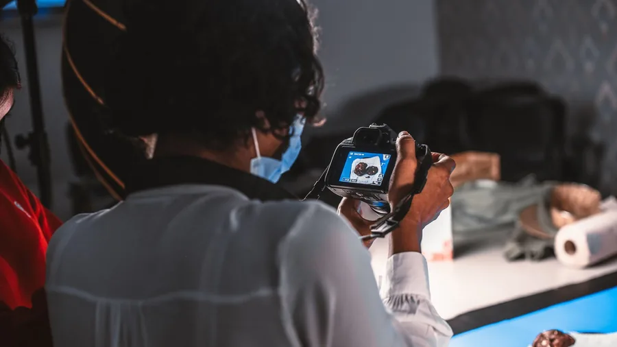Eine Fotografin richtet im Studio eine Kamera auf ein Produkt auf einem weißen Tisch