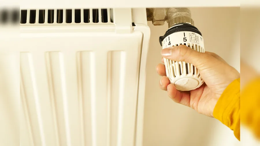 Eine Hand dreht den Thermostatkopf an einem weißen Heizkörper, auf der Skala sind die Stufen 4 und 5 zu sehen