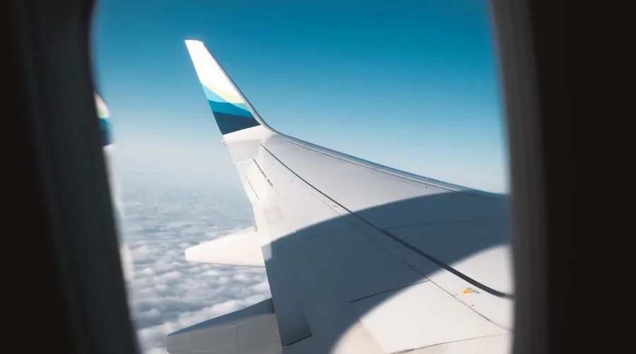 Blick aus dem Flugzeugfenster auf die Tragfläche über einer Wolkendecke
